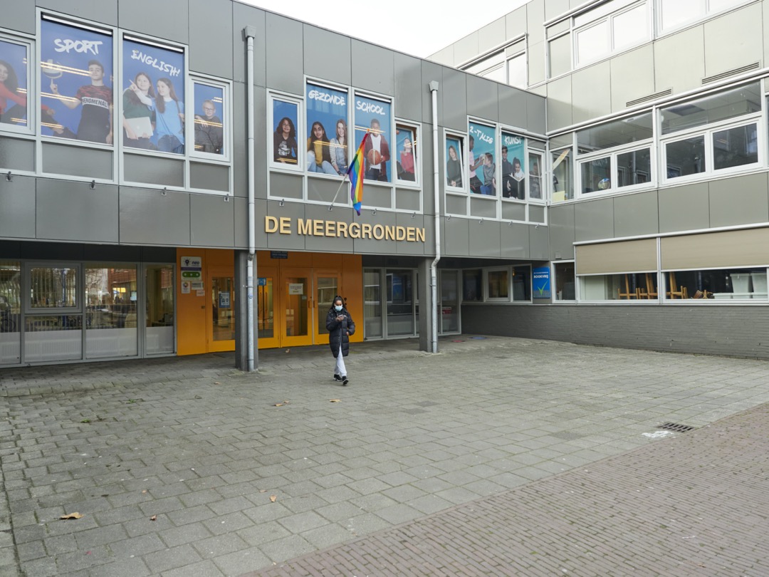 Foto van de ingang van schoolgebouw de Meergronden met een leerling met een mondkapje op.
